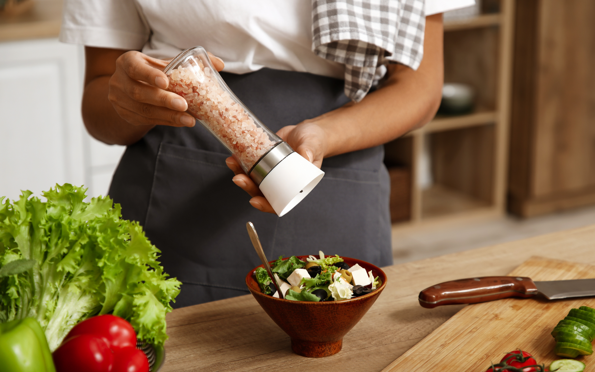 Person adding pink salt to a fresh salad in a kitchen, illustrating salt for fasting and electrolyte support during meal planning.